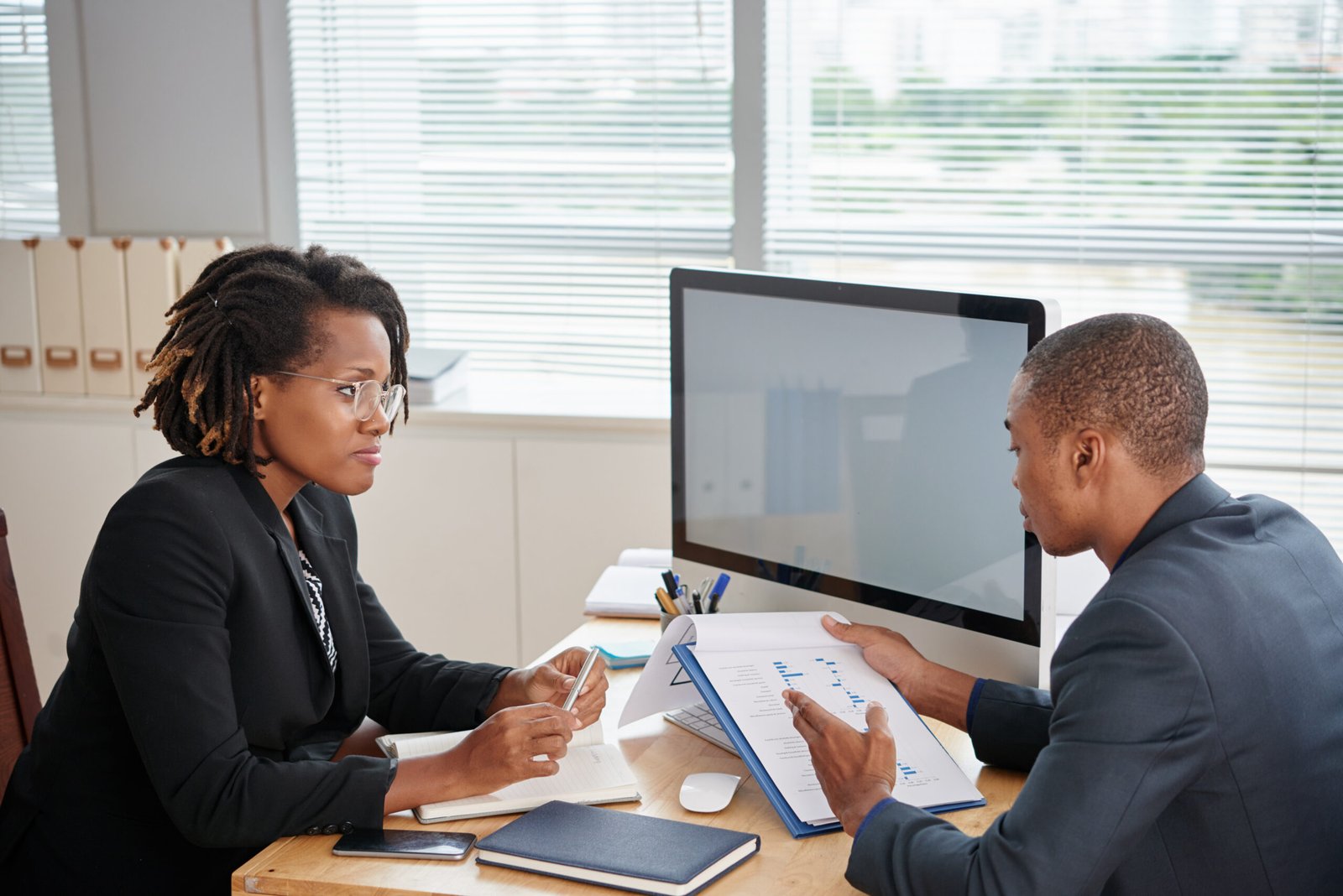 afro american man suit holding documents talking female boss scaled